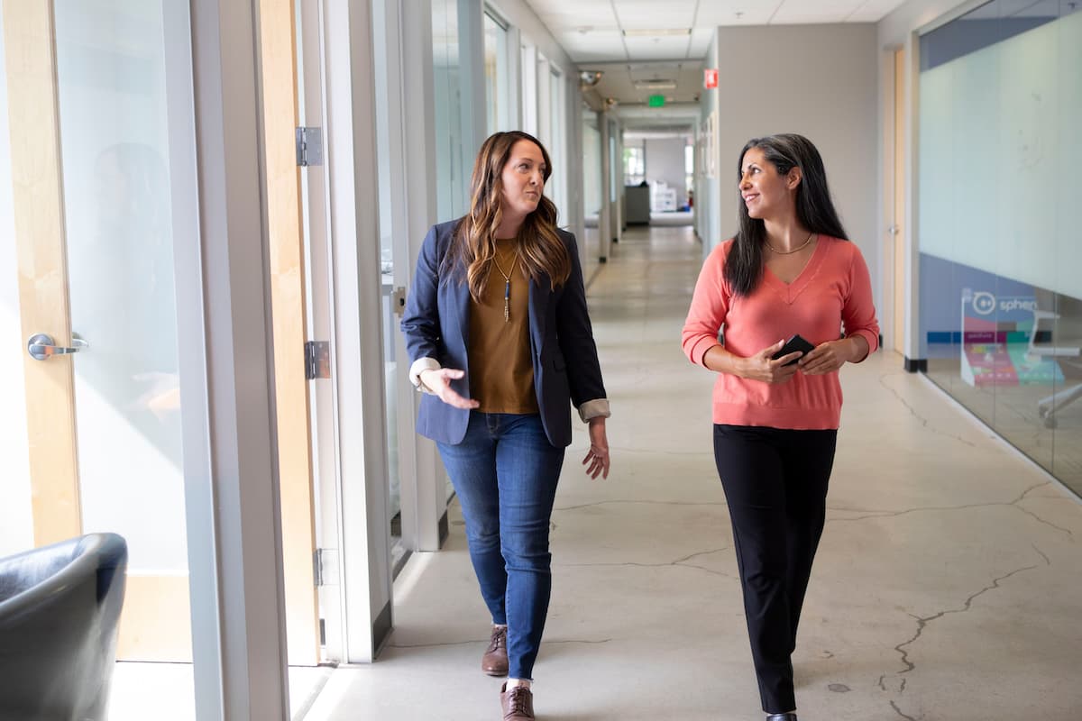 Two colleagues taking a walking break together in an office hallway