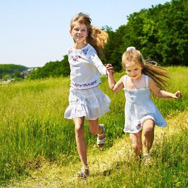 2 smiling girls holding hands and running outdoors through long grass