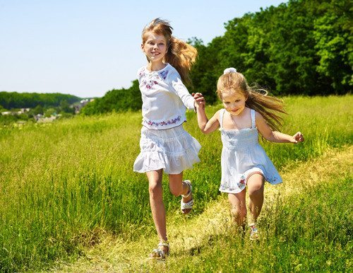 2 smiling girls holding hands and running outdoors through long grass