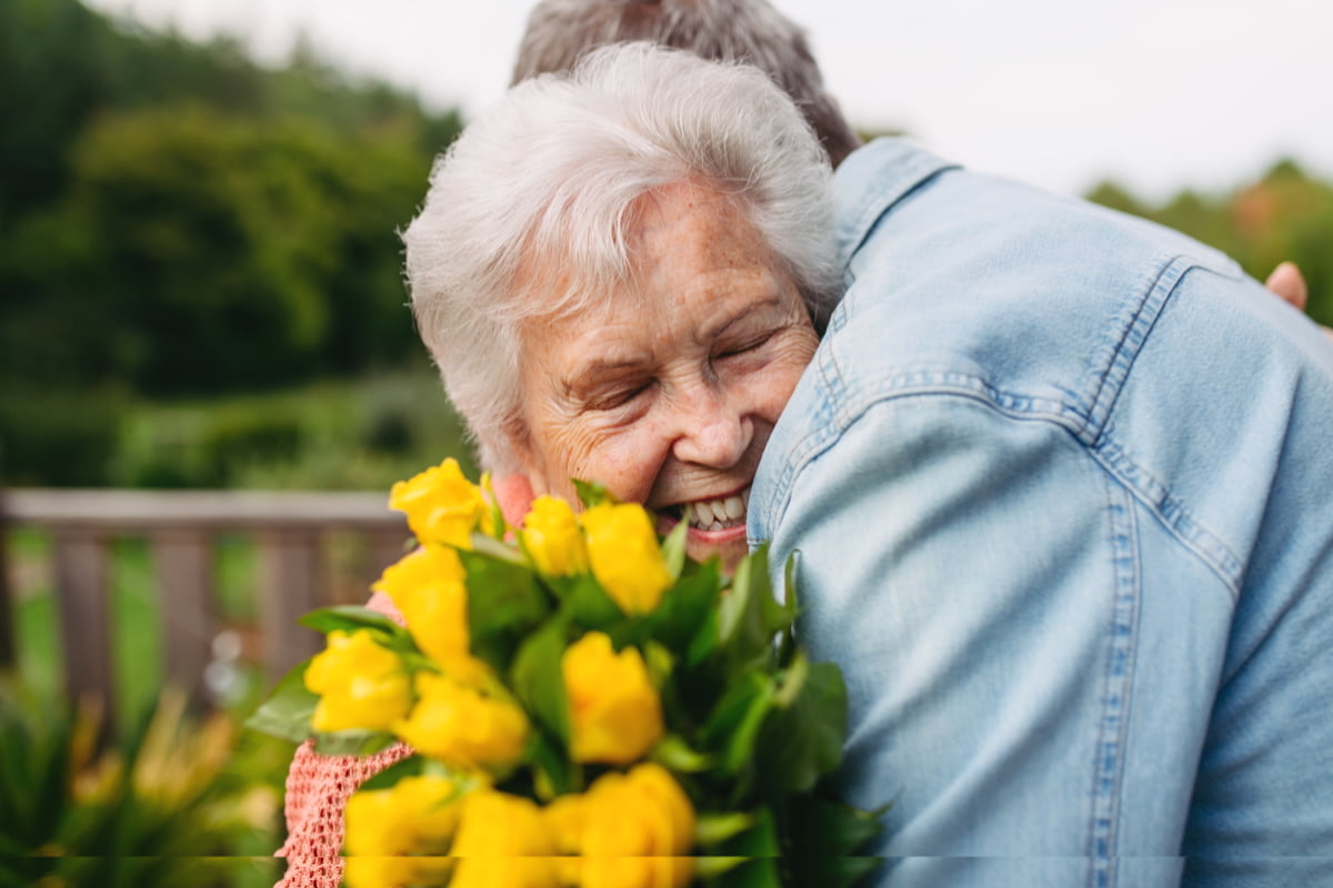 Elderly mother holding flowers and hugging adult child, showing emotional support and social connection
