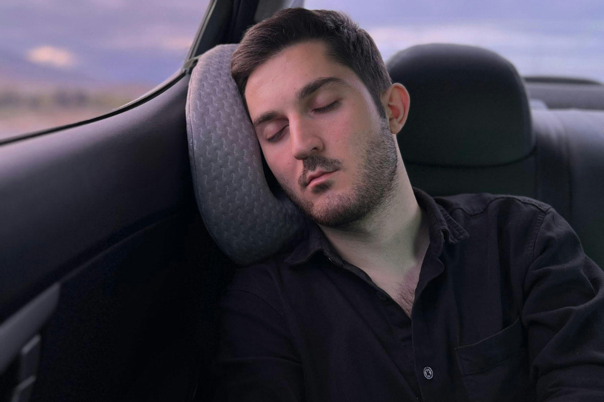 Man power napping in a car seat with a travel pillow, illustrating practical daytime power napping techniques
