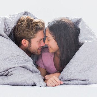 smiling man and woman nose to nose under a duvet together