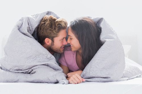 smiling man and woman nose to nose under a duvet together